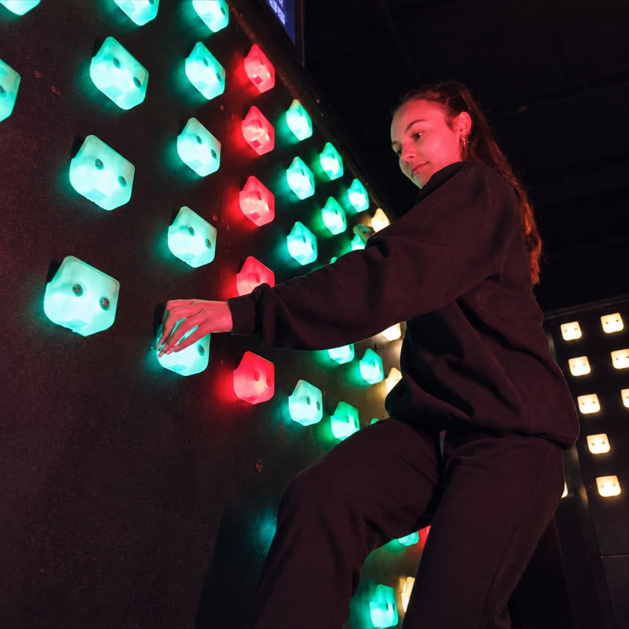 Joueuse sur les prises lumineuses du mur d’escalade interactif CLIMB